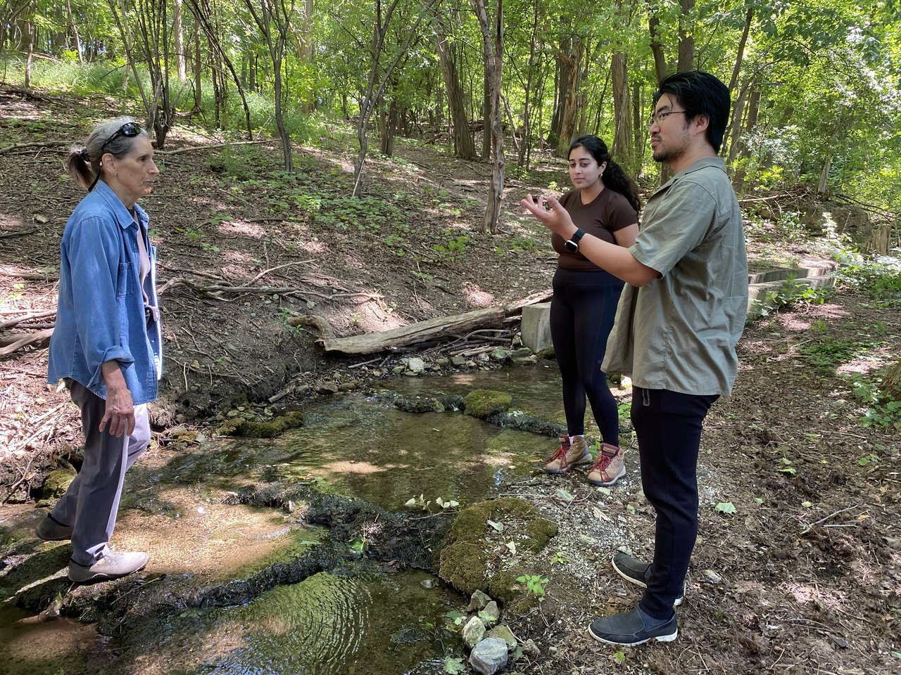 Three people talking beside a stream.