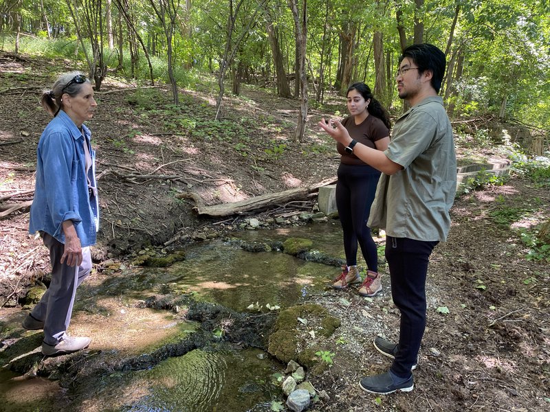 Three people talking beside stream.