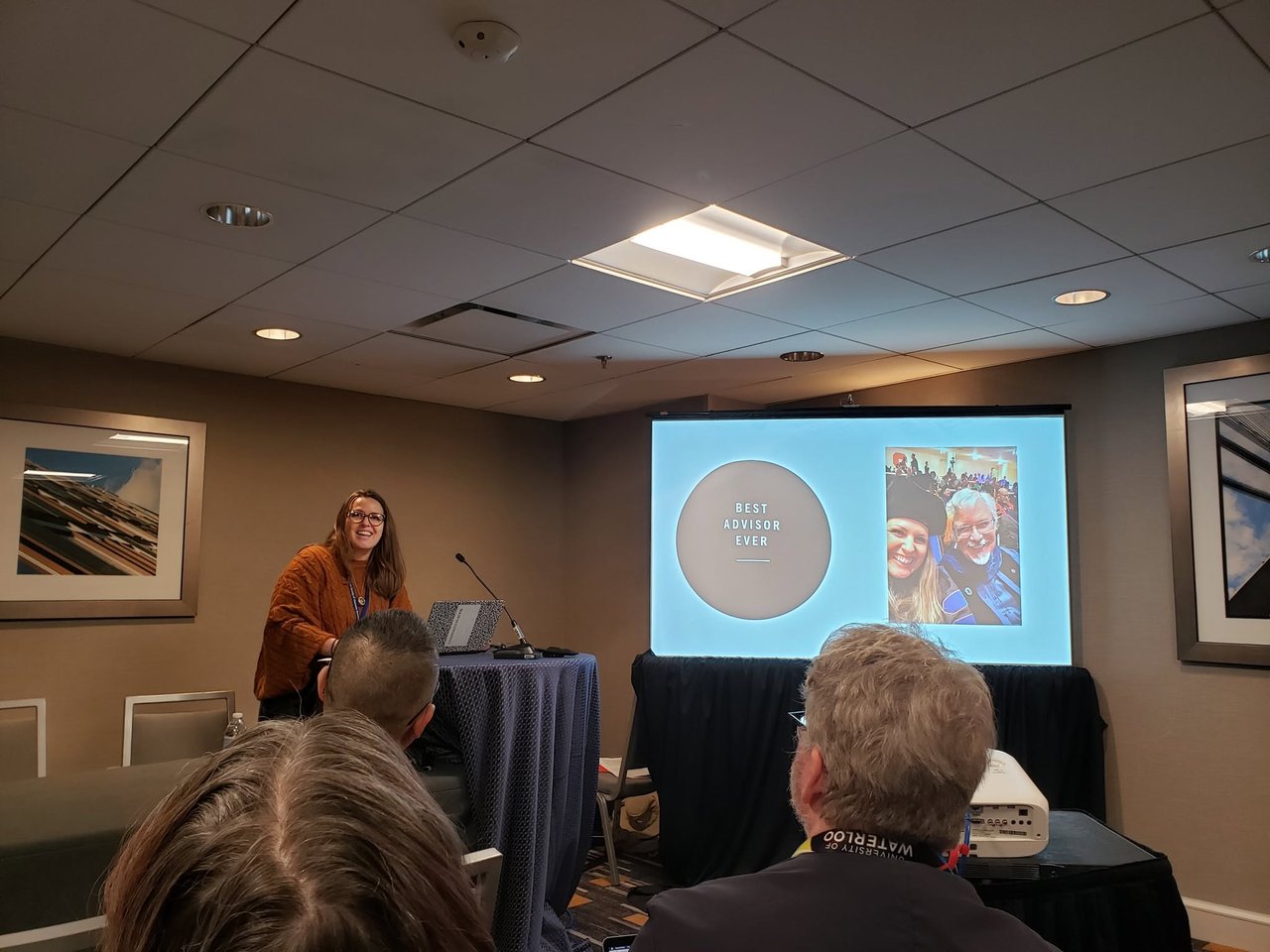 Person presenting in a room to a group of people.