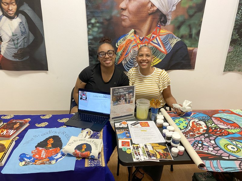 Two people seated behind a table of art supplies.