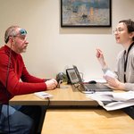 "A speech-language pathologist at the Syracuse University Aphasia Lab works with a stroke survivor wearing a transcranial direct current stimulation device on his head, as the two sit across a table during a language therapy session.