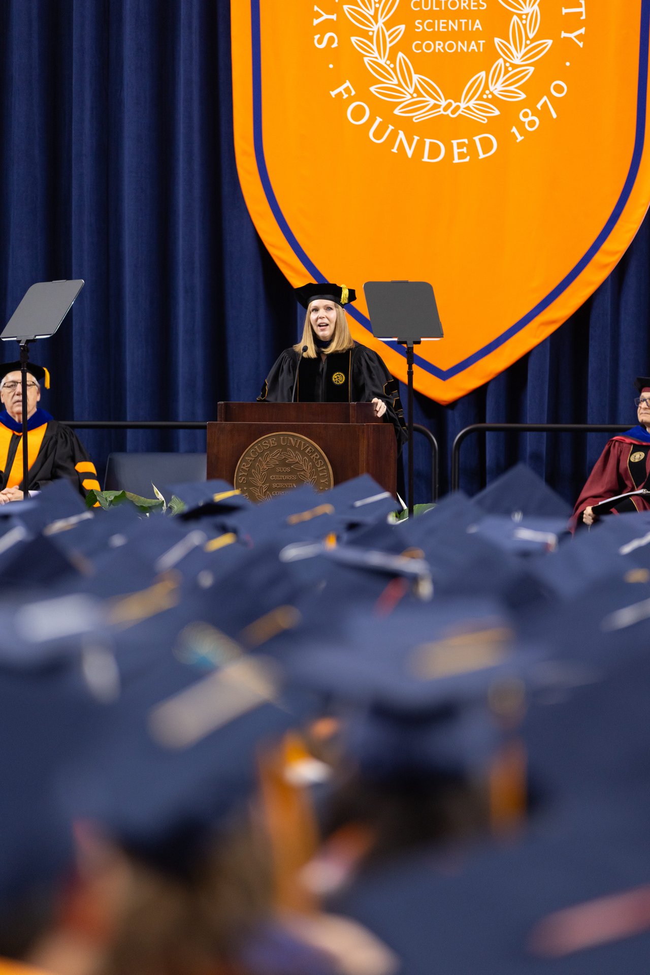 A faculty speaker in academic regalia at a podium.