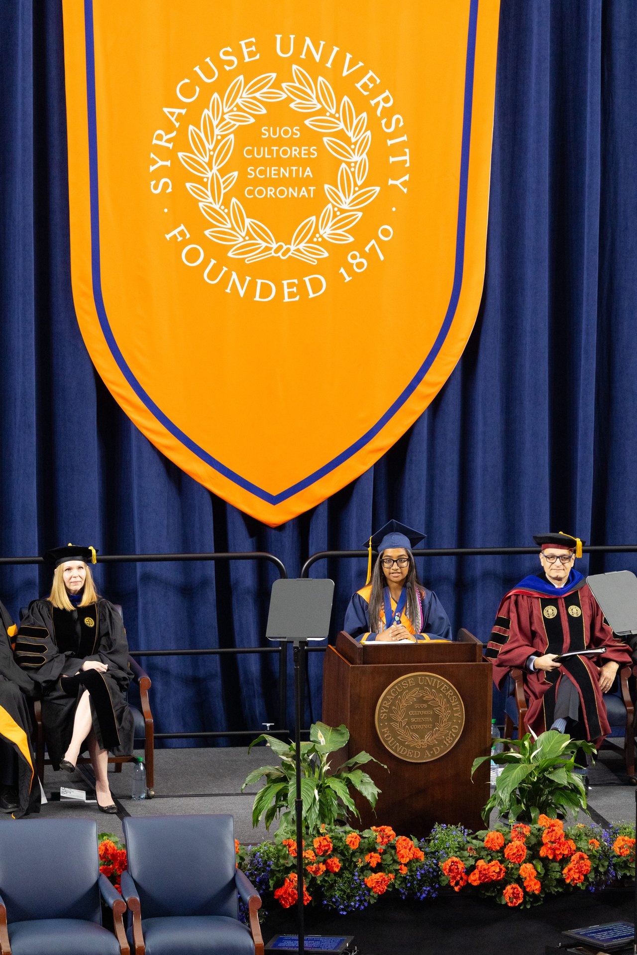 A student in graduation regalia speaks at a podium.