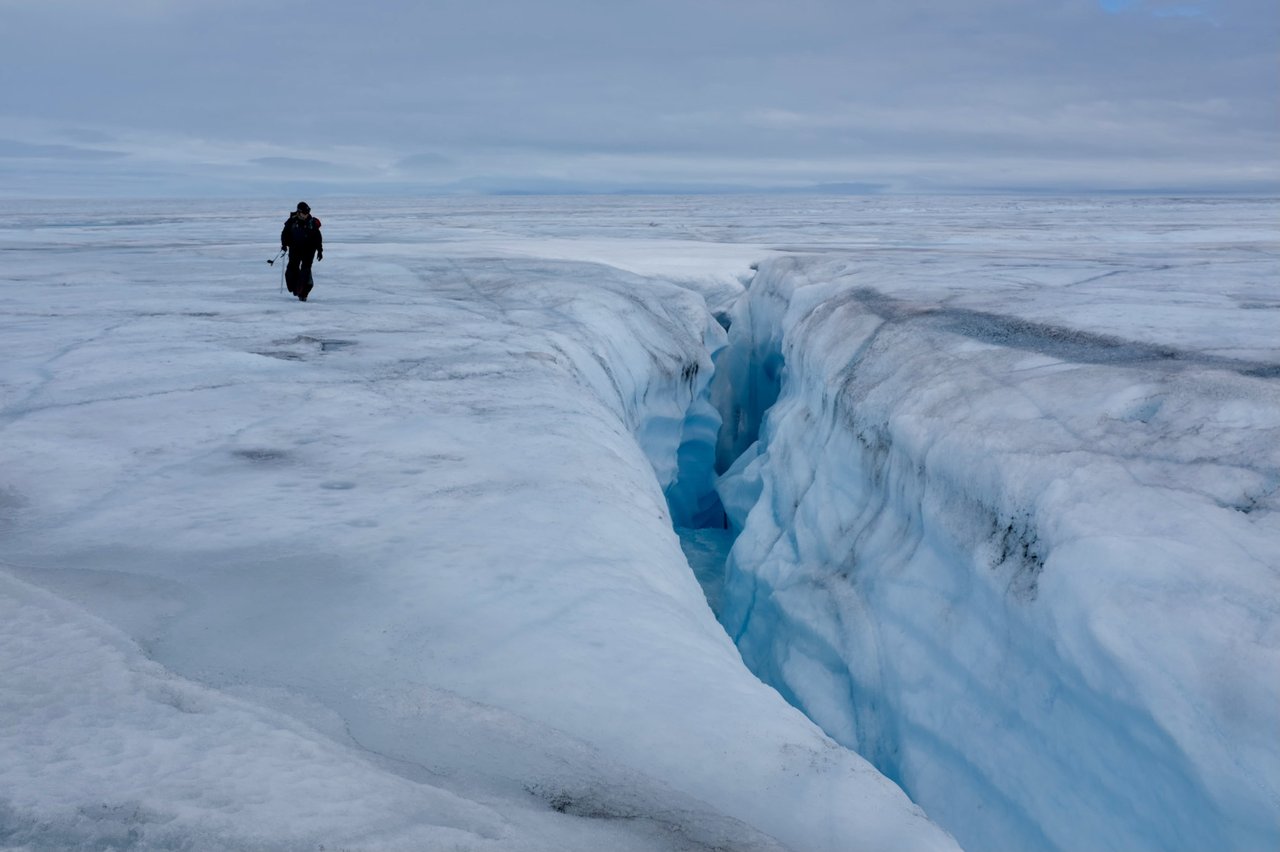 Person standing next to a supraglacial stream in an ice sheet.