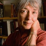 Woman standing in a room with books on a bookshelf in the background.