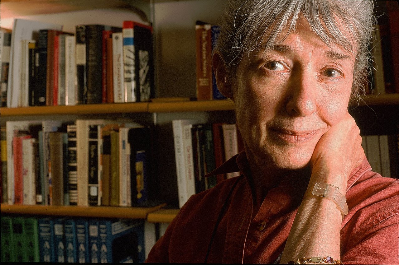 Woman standing in a room with books on a bookshelf in the background.