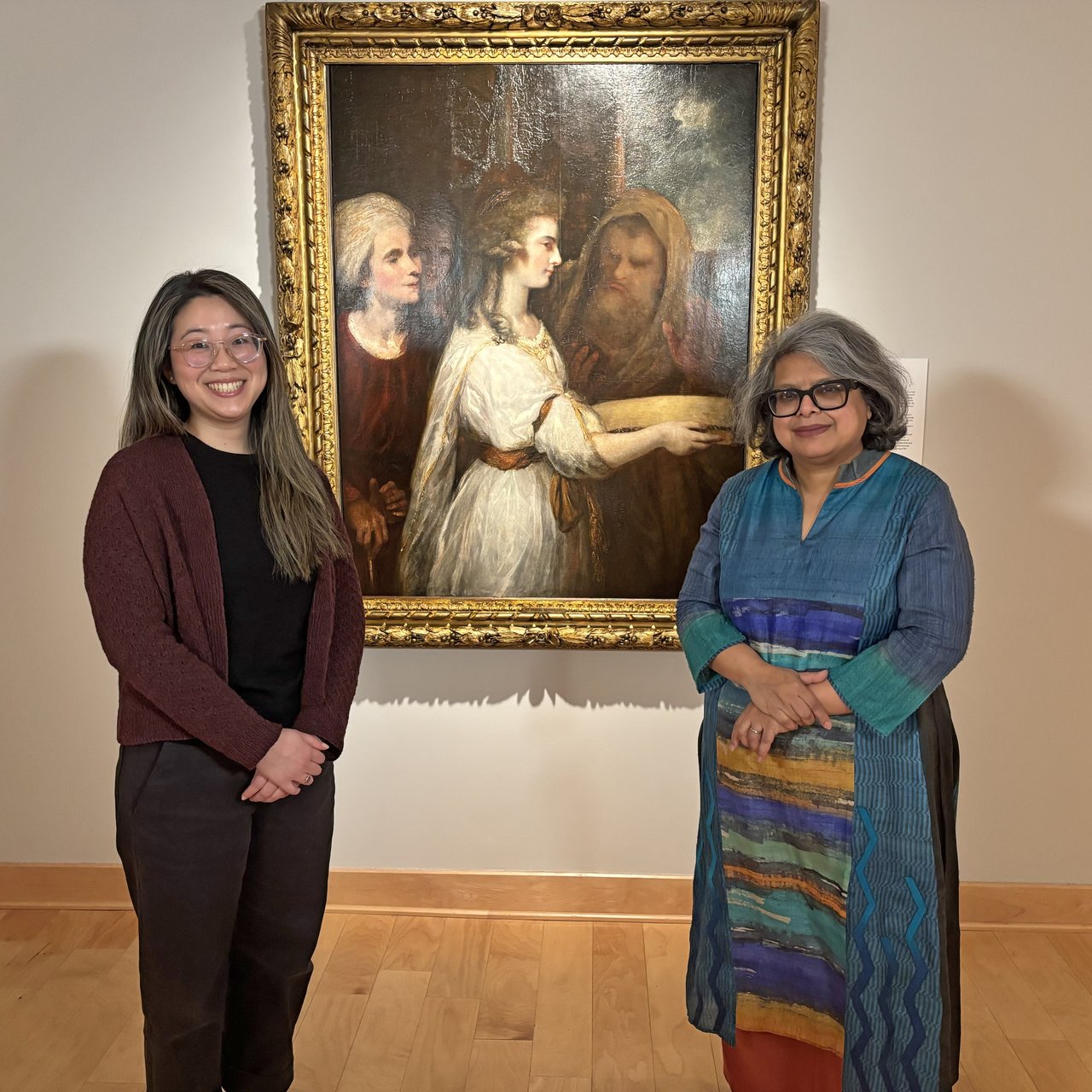 Two women standing in front of a painting.