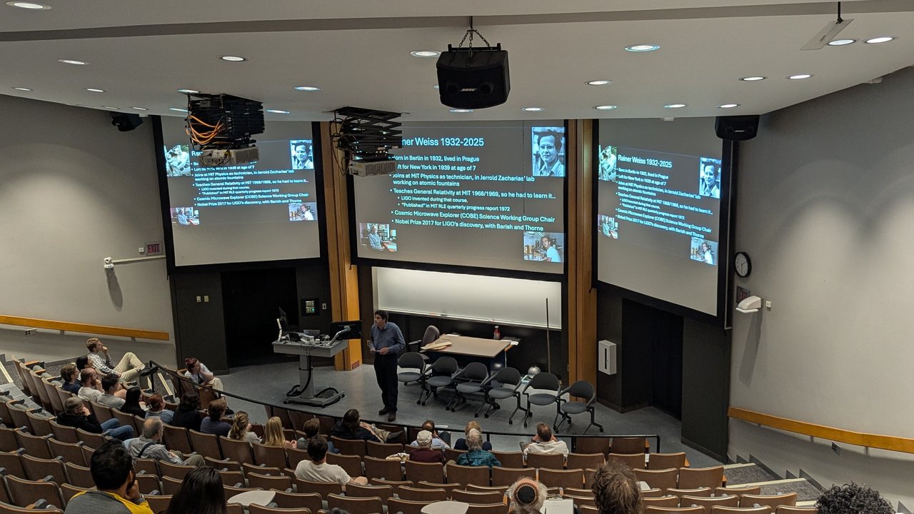 Person speaking to a room of people with three projector screens in the background.