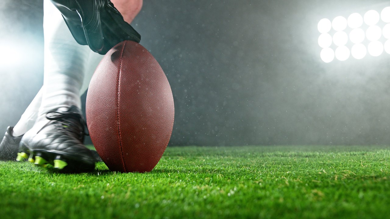 A foot kicking a football being held by a finger.