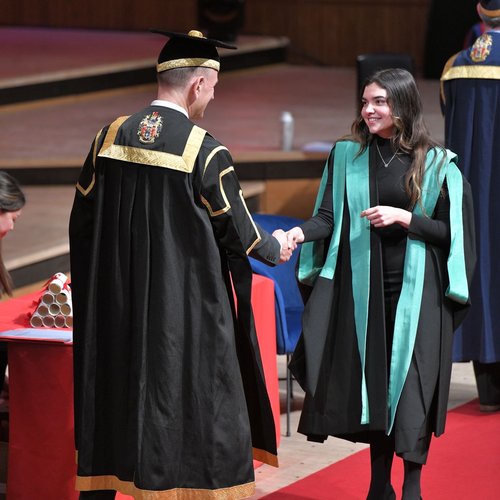 Person walking across a stage shaking hands with another person.