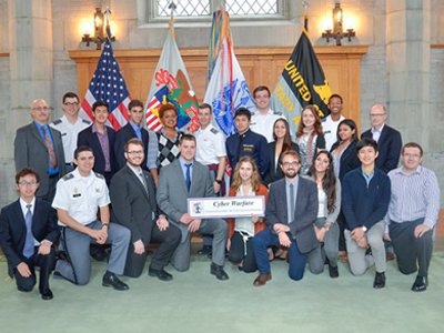 Hackett (center left, kneeling with sign) shown with his Cyberwarfare roundtable group. 