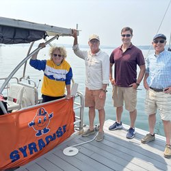 Group of people standing on a dock with a boat and lake in the background.