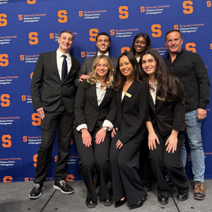 Group of people standing in front of a Syracuse University Whitman School banner.