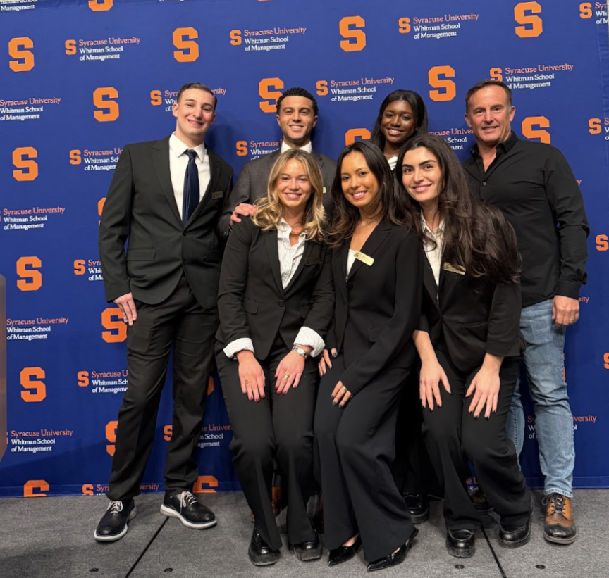 Group of people standing in front of a Syracuse University Whitman School banner.