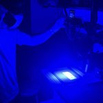 Person using a camera and blue light to capture prints on currency.