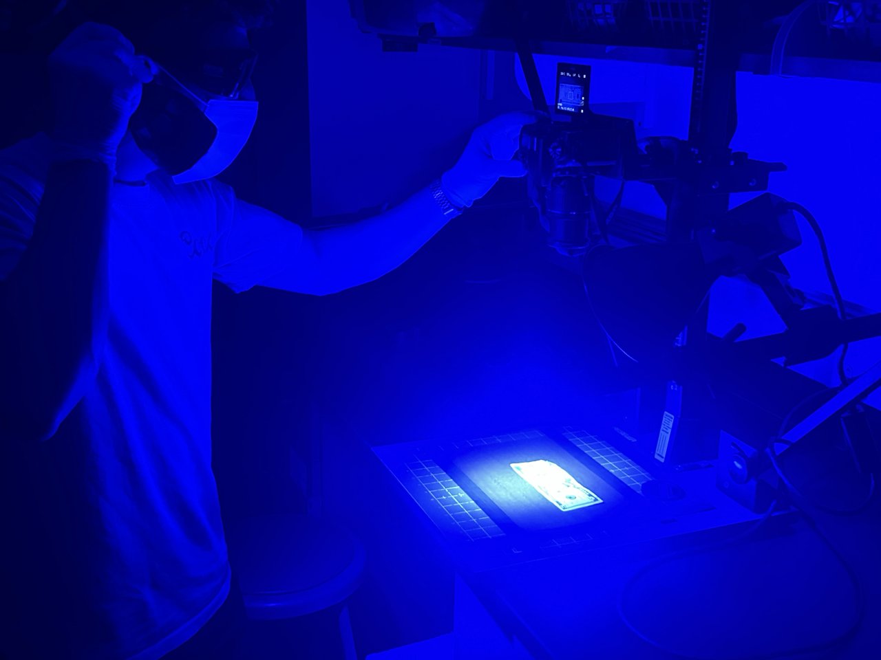 Person using a camera and blue light to capture prints on currency.