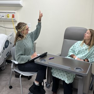 One person holding up a finger and another person looking up while seated in a simulated medical lab.
