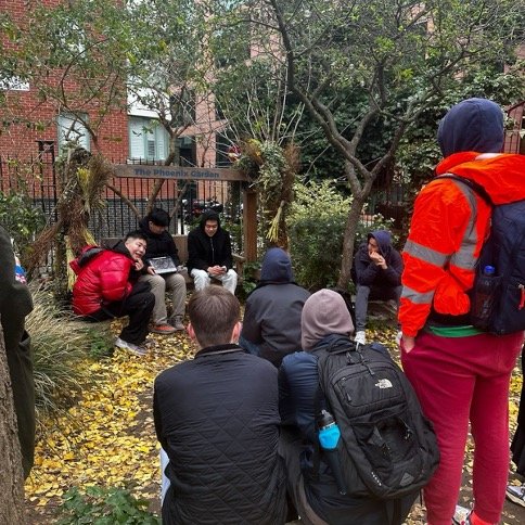 Group of students seated in a park.Students from Syracuse London’s Sustainable Urbanism course examining the role of community-driven spaces in urban sustainability at Phoenix Garden in London. According to the Phoenix Garden website, it “provides a green retreat from the stresses of the city and a valuable habitat for urban wildlife.z