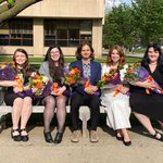 Five students sitting with flowers on a  bench.