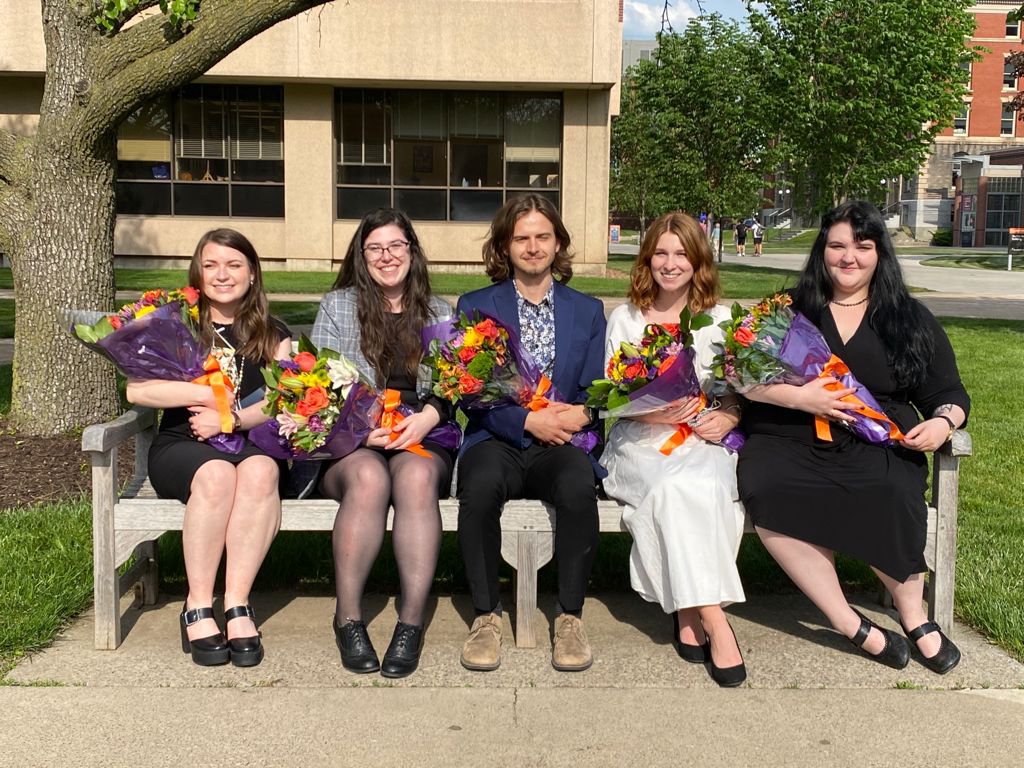 Five students sitting with flowers on a  bench.