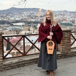 A woman holding a stringed instrument with a city in the background.