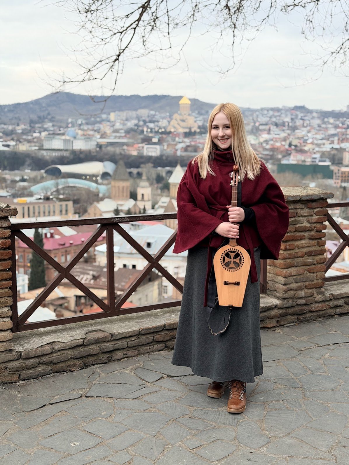 A woman holding a stringed instrument with a city in the background.