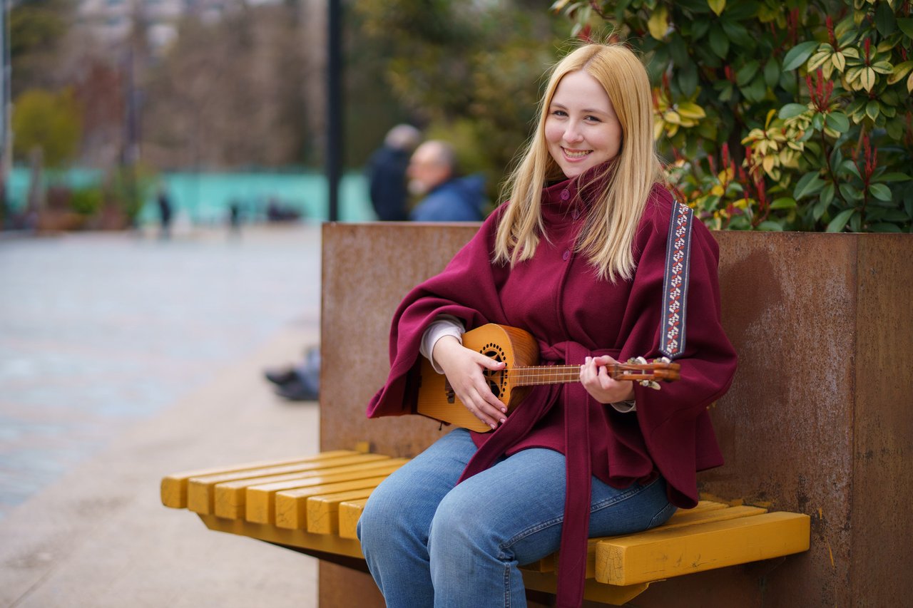 Person holding a stringed instrument sitting on a bench.