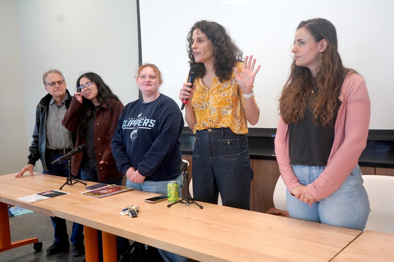Five people taking part in a panel and standing behind a table.