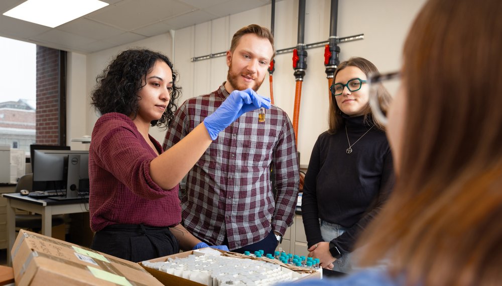 Woman holding vial while two other people look on.