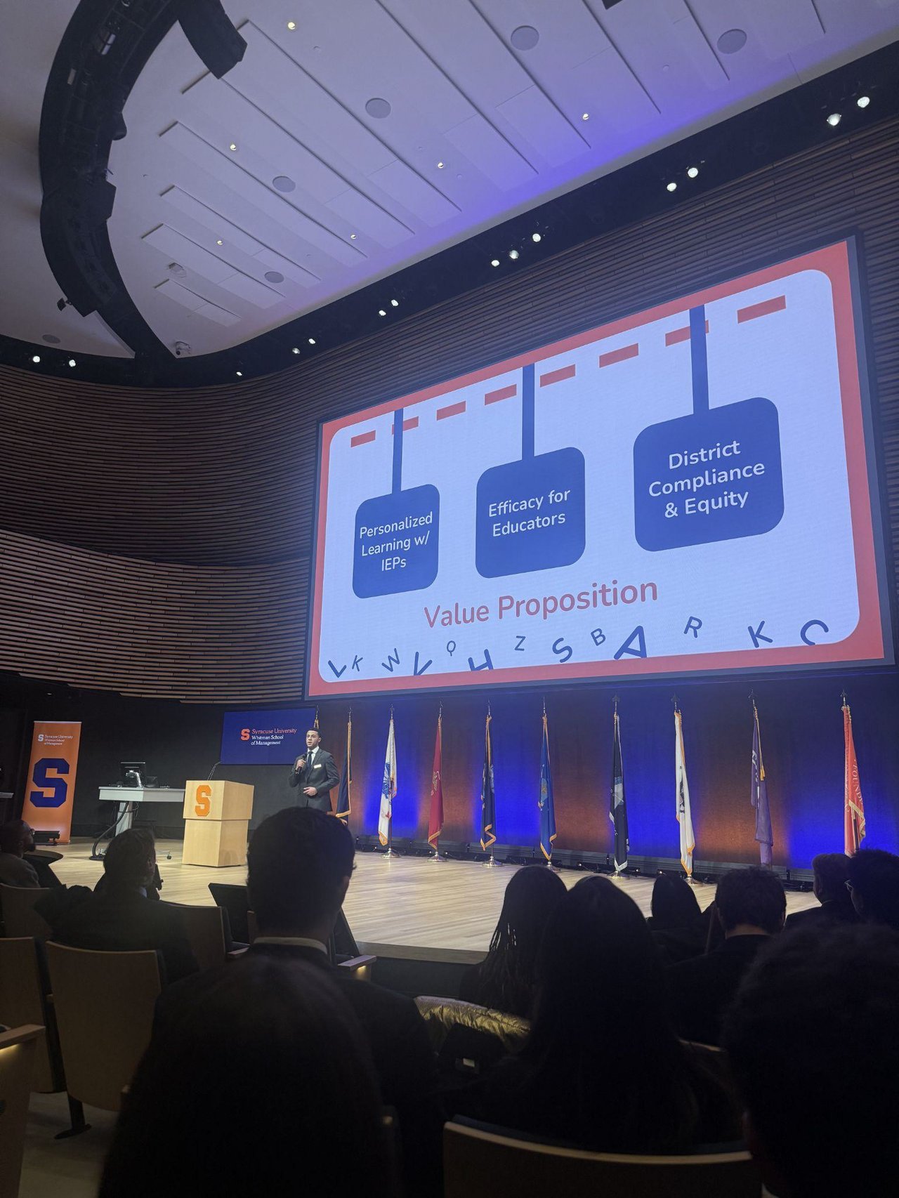 Person presenting on a stage to a group of people.