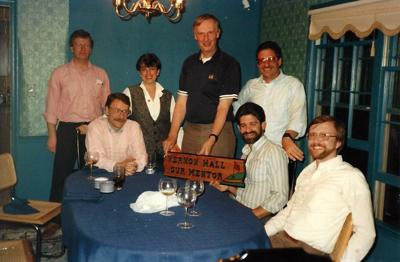 Group of people standing and sitting around a table.