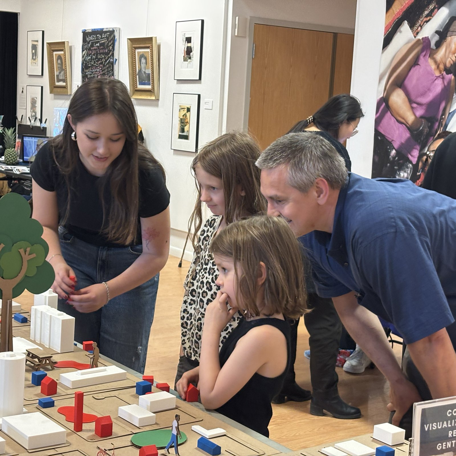 Adults and children standing around a scale model.