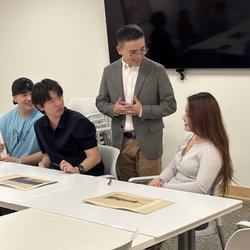 One person standing and three sitting discussing photographs.