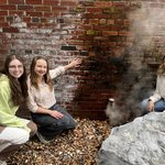 Three women bending down in front of a steam vent.