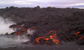 Incandescent orange lava magnifies cracks in the black outer crust. Steam formed when the lava flowed into a nearby river.
