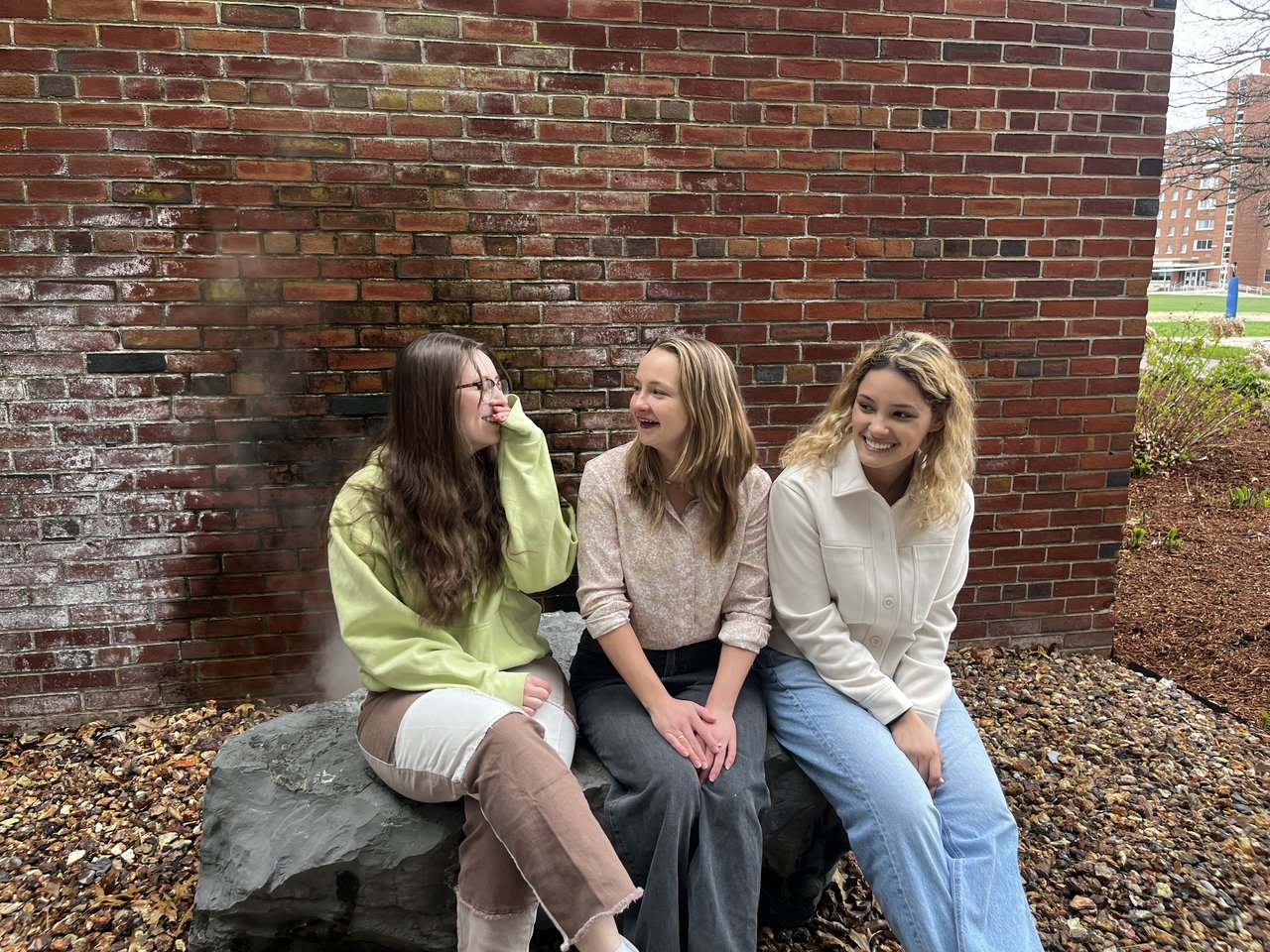Three people sitting and laughing together in front of a steam vent.
