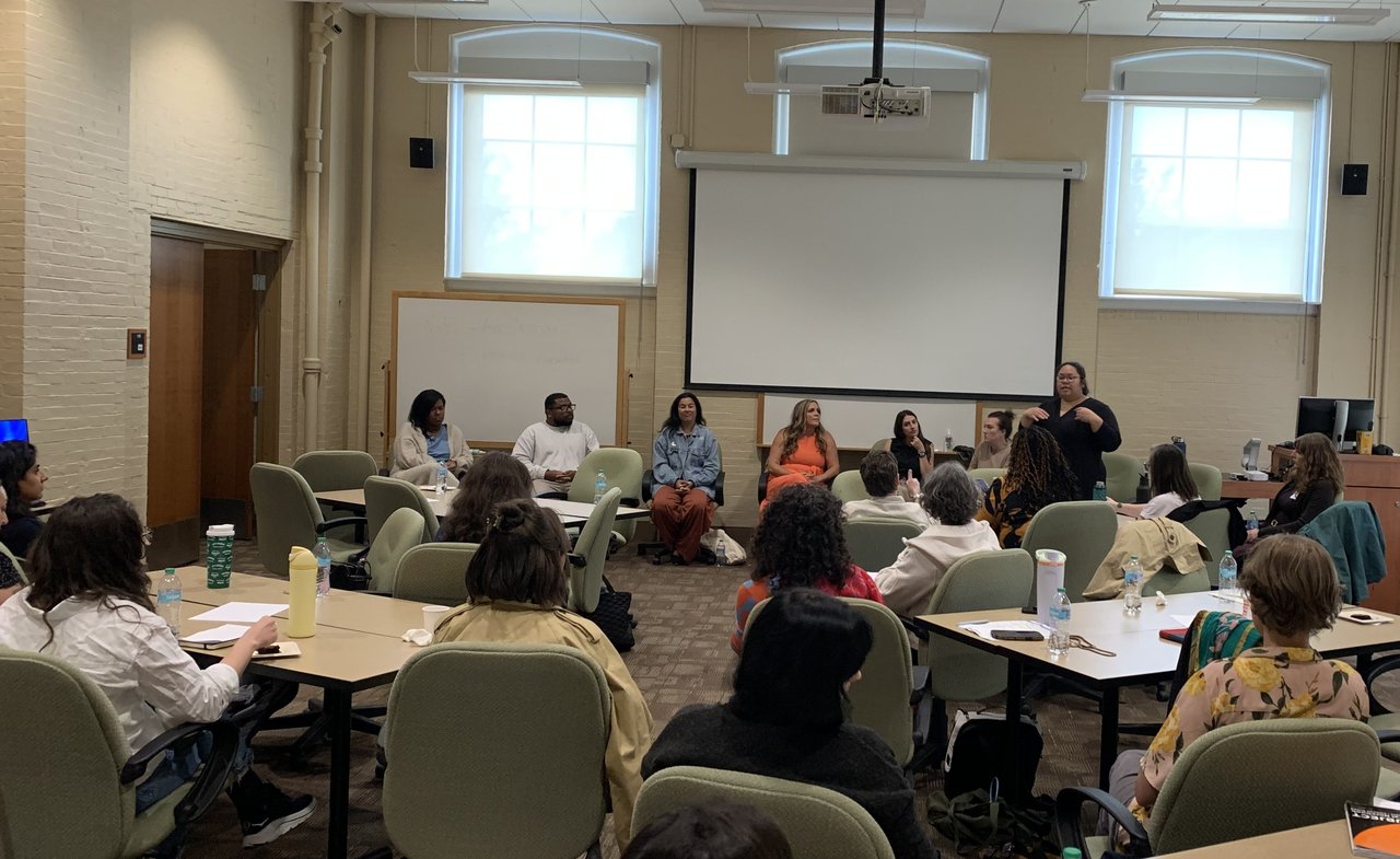 A panel speaks before a room of master's students.